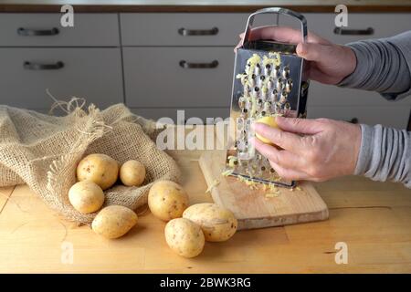 Les mains d'une femme sont râper des pommes de terre avec un râleur en métal sur une table de cuisine en bois, foyer choisi, profondeur de champ étroite Banque D'Images