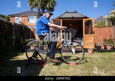 Un homme âgé dans ses années 80 qui garde la forme sur un vélo d'entraînement se trouve dans son jardin à l'arrière pendant le confinement du coronavirus, dans le sud-ouest de l'Angleterre, au Royaume-Uni Banque D'Images