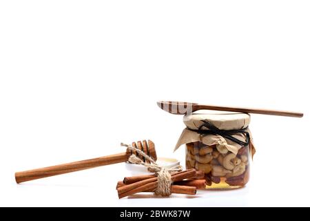 Composition du village d'été. Pot rempli de noix de cajou et d'amandes près du miel isolé sur fond blanc. Concept de récolte des agriculteurs. Noix et soucoupe au miel, couchés par des cuillères en bois et des bâtons de cannelle Banque D'Images