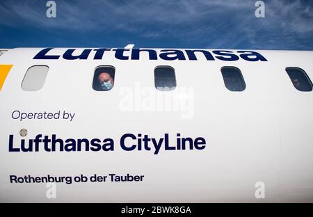 02 juin 2020, Rhénanie-du-Nord-Westphalie, Münster : un passager regarde par la fenêtre d'un avion de Lufthansa avec son masque de protection de la bouche et du nez. Après le blocage des opérations de vol provoqué par la couronne à l'aéroport de Münster-Osnabrück, Lufthansa repart avec sa liaison avec Munich. AIS-Airlines suivra la route vers Stuttgart. Les premiers vols touristiques sont attendus à la fin du mois de juin au début des vacances d'été en Rhénanie-du-Nord-Westphalie. Photo: Guido Kirchner/dpa Banque D'Images