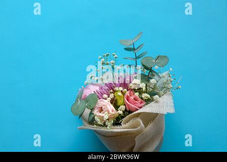 Le bouquet de fleurs de la main se compose de chrysanthème, de roses et de feuilles vertes sur fond bleu. Copier l'espace. Banque D'Images