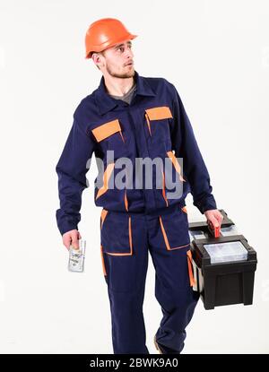 Homme avec des promenades à outils, tient de l'argent. Builder sur le visage suspect strict dans le casque sur fond blanc. Le constructeur tient de l'argent, le réparateur garde de l'argent, les billets en main. Concept de construction et de reprise. Banque D'Images