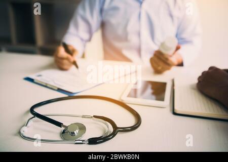 Médecin confiant, homme tenant une bouteille de pilule et écrivant tout en parlant avec le patient âgé et en examinant son médicament dans la salle de bureau. Banque D'Images