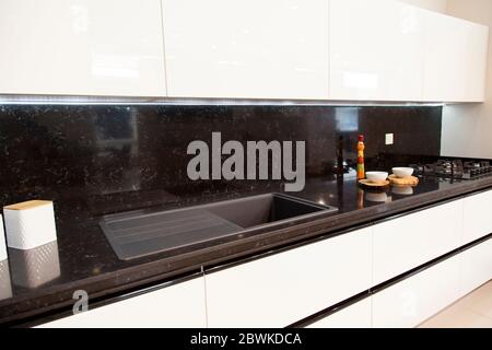 Intérieur de cuisine moderne luxueuse, armoires blanches en granit noir et évier acrylique Banque D'Images