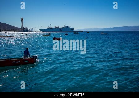 Aqaba, Jordanie - 2 février 2020 : le pêcheur revient à la terre en petit bateau à moteur après avoir pêché dans la mer Rouge. Grand bateau de croisière en arrière-plan. Ciel clair et sans nuages jour d'hiver. Cadre horizontal Banque D'Images