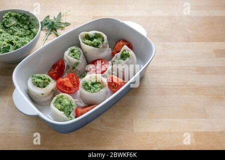 Rouleaux de poisson de filets de plie remplis de céleri et d'arugula écrasés, placés avec des tomates dans un plat à cocotte sur un plan de travail en bois, cuisant un méa léger Banque D'Images