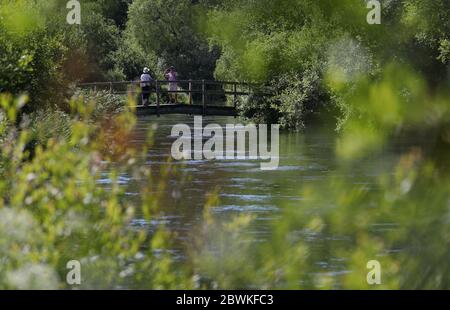 Deux personnes traversent un pont sur la rivière Itchen, près d'Ovington dans le Hampshire, alors que l'on rappelle au public de pratiquer la distanciation sociale après le relâchement des restrictions de verrouillage en Angleterre. Banque D'Images