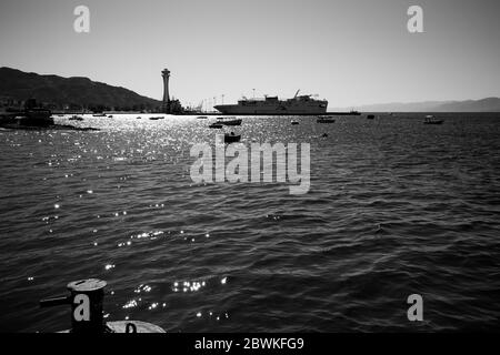 Image de contré-jour noir et blanc du Moyen-Orient Port industriel de la mer Rouge avec phare de la tour de contrôle, Aqaba, Jordanie. Le ferry s'amarre dans l'après-midi ensoleillé d'hiver sans nuages Banque D'Images