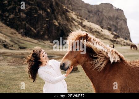 Destination Islande mariage séance photo avec des chevaux islandais. Une mariée vêque d'une robe blanche se fond le nez d'un cheval. Les cheveux et la manie se développent dans le vent. Banque D'Images