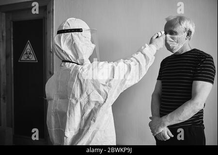 Aperçu noir et blanc de la visite du médecin au domicile du patient pendant la quarantaine 2020. Image de l'arrière du médecin mesurant la fièvre de l'homme ancien avec un thermomètre infrarouge sans contact. Concept de coronavirus Banque D'Images