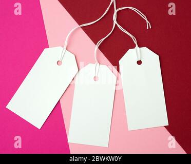 trois étiquettes rectangulaires en papier blanc sur une corde sur un fond coloré, plat. Étiquette de prix, cadeau, pour l'adresse écrite Banque D'Images