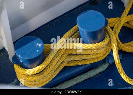 corde de bateau jaune attachée autour des bornes bleues d'amarrage sur un pont de bateau en métal Banque D'Images