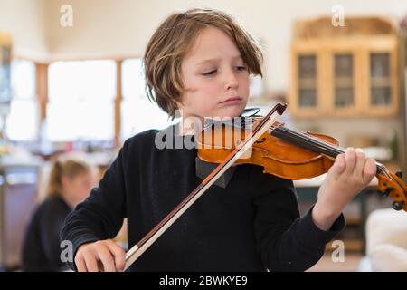 Garçon de six ans jouant du violon, ayant une leçon vidéo à distance en verrouillage à la maison. Banque D'Images