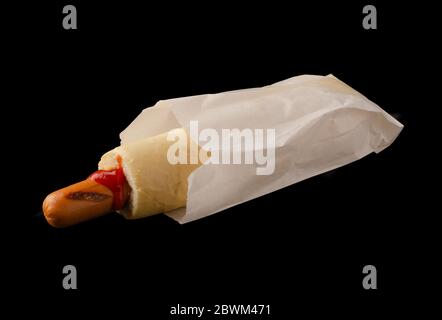 Hot-dog français dans un petit pain grillé servi avec du ketchup et de la moutarde dans un emballage en papier isolé sur fond noir Banque D'Images
