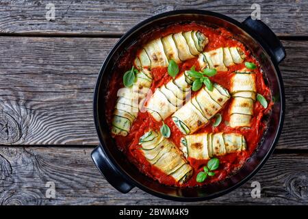 Roulés de courgettes farcis à la ricotta italienne fraîche avec des feuilles d'épinards et de basilic, ail cuit dans la sauce tomate, servi sur un plat de cuisson noir sur rus Banque D'Images