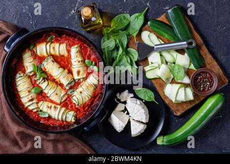 Courgettes courgettes farcies à la ricotta au fromage frais italien avec de jeunes épinards et des feuilles de basilic cuites dans une sauce tomate servies sur une plaque de cuisson noire Banque D'Images