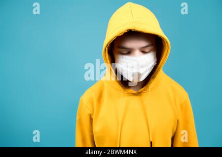 adolescent dans un sweat-shirt jaune sur un fond bleu avec un bandage médical sur son visage regarde vers le bas. Copier l'espace Banque D'Images