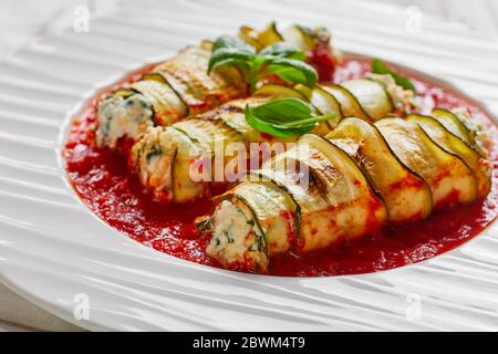 Une portion de courettes de courgettes au fromage ricotta italien peu gras mélangé avec des jeunes épinards frais cuits dans une sauce tomate sur une assiette avec une feuille de basilic frais o Banque D'Images