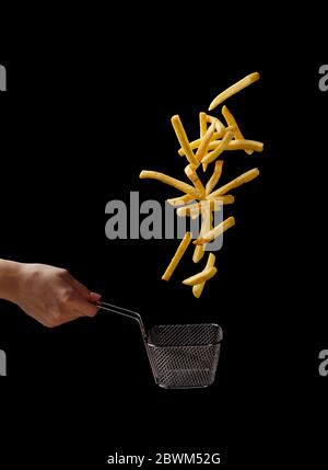 Frites - pommes de terre frites sortant du panier à la main, fastfood à la mouche isolé sur fond noir Banque D'Images