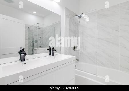 Une salle de bains principale entièrement blanche avec quincaillerie noire et robinets montrant la coiffeuse et la douche avec la porte ouverte. Banque D'Images