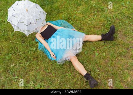 Femme en grandes bottes noires et une jupe bleue repose sur l'herbe verte. Concept après la fête Banque D'Images