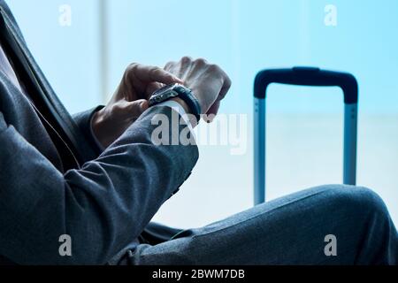 gros plan d'un jeune homme d'affaires, en costume gris, assis dans le hall d'attente d'un aéroport ou d'une gare, en regardant son montre-bracelet Banque D'Images