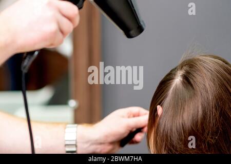 Les mains du coiffeur soufflent les cheveux de la femme au salon de beauté. Banque D'Images