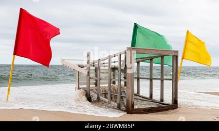 L'océan est en train de dépasser la terre sous un stand de sauveteurs qui est situé sur le sable avec des drapeaux rouges, jaunes et verts à côté. Banque D'Images