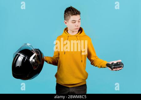 L'adolescent tient un joystick modifié sans marques d'identification et un casque de moto dans ses mains, en choisissant un joystick. Le choix entre réel Banque D'Images