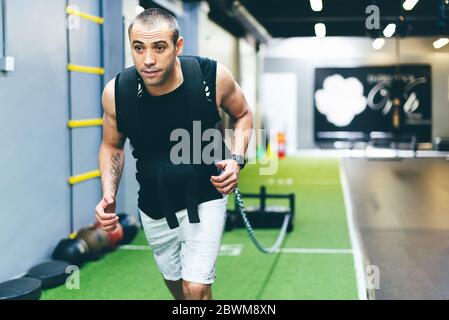 Latin garçon faisant de l'exercice physique en salle de gym traînant un traîneau avec le poids. Concept de formation Banque D'Images