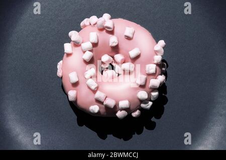 Vue de dessus de délicieux donat rose avec guimauves blanches sur l'assiette en céramique gris foncé. Concept macro de la nourriture sucrée de Creartive. Isolé lumineux Banque D'Images