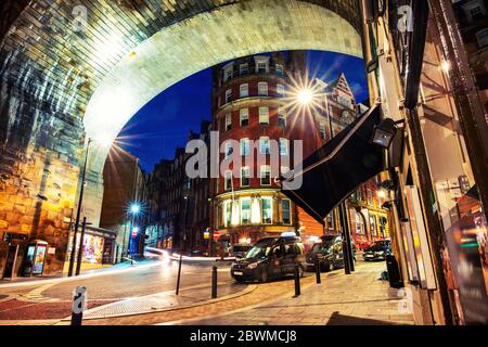 Newcastle Upon Tyne, au Royaume-Uni. Sous le pont Tyne dans la nuit. Monuments illuminés à Newcastle, UK avec cafés, restaurants, boutiques et voitures de taxi Banque D'Images