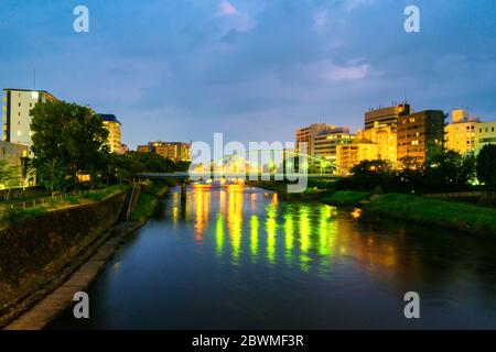 Kumamoto, Japon. Vue sur un pont au-dessus de la rivière Shirakawa à Kumamoto, Japon pendant la nuit avec des gratte-ciels Banque D'Images