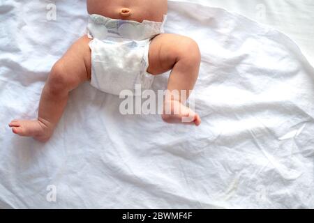 Les jambes de bébé et le bas en couche sur fond de lit blanc, vue du dessus, copy space Banque D'Images