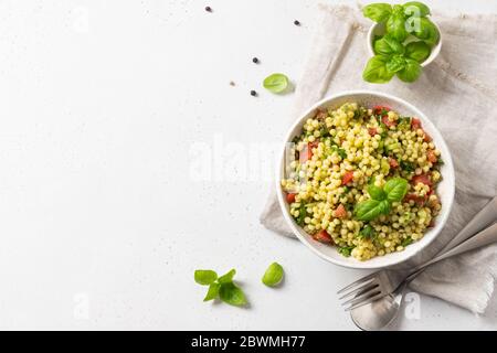Salade de légumes avec pâtes ptitim ou Birdy, feuilles de basilic au décor israélien couscous sur fond blanc. Vue de dessus. Banque D'Images