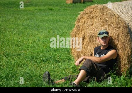 Homme fatigué assis sur la balle de foin et d'herbe, vue d'été Banque D'Images