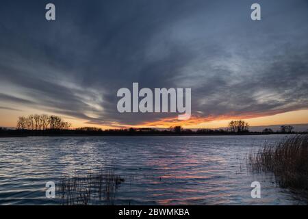 Des nuages fantastiques dans le ciel après le coucher du soleil sur un lac calme avec des roseaux Banque D'Images