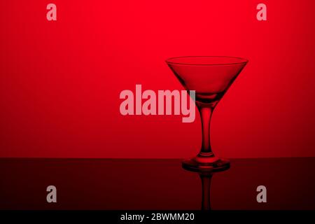 Gobelet en verre sans vin sur une jambe mince se tient sur une surface miroir. Rétroéclairage. Arrière-plan rouge. Banque D'Images