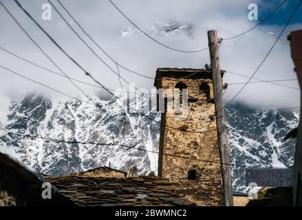 Ancienne tour traditionnelle de RamManille et maison de machin avec pierre de pavillon et poteau en bois avec beaucoup de fils électriques contre la montagne de neige, Svane supérieure Banque D'Images