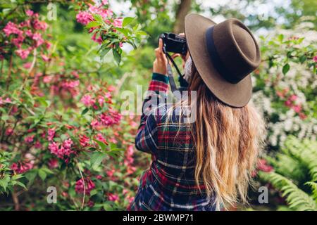 Femme photographiant des fleurs avec un appareil photo numérique dans un jardin d'été. Fille marchant appréciant le passe-temps dehors Banque D'Images