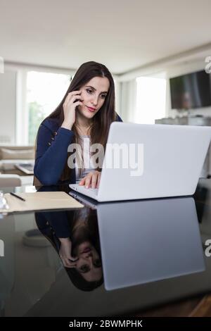 Femme d'affaires parlant sur le smartphone et utilisant un ordinateur portable à la maison. Concept de travail à distance. Banque D'Images