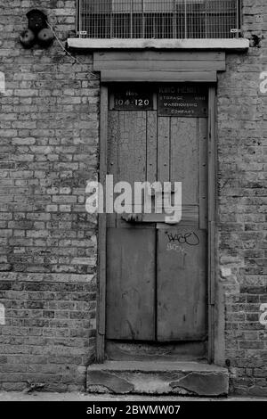 Ancienne porte d'entrepôt en état de délabrement située dans les docklands de Londres. Boulonné et verrouillé. En noir et blanc Banque D'Images