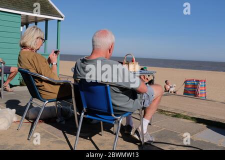 un couple plus âgé assis au café sur la plage regardant leurs téléphones sans vue sur la mer Banque D'Images