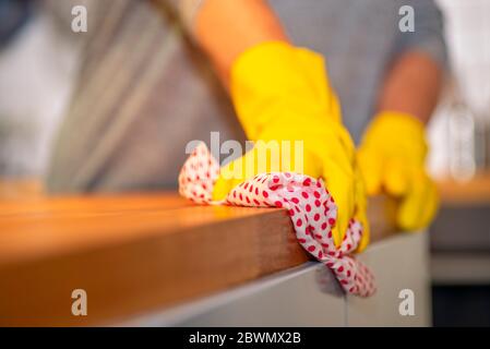 Personne avec des gants en caoutchouc jaune essuie avec un chiffon sur un plan de travail dans une cuisine Banque D'Images