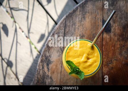 Jus de mangue en verre avec paille en métal sur la table dans le café tropical, vue de dessus Banque D'Images