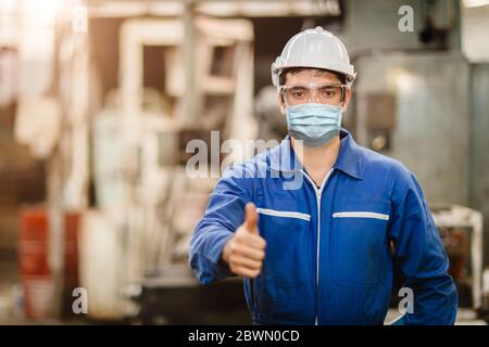 Un travailleur portant un écran facial ou un masque facial jetable pendant le travail en usine pour prévenir la pollution par le coronavirus (Covid-19) ou la poussière d'air en usine Banque D'Images