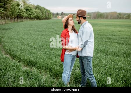 Portrait d'une femme enceinte avec son petit ami vêtu de façon décontractée avec des chapeaux debout ensemble sur le terrain vert. Un couple heureux attend un concept de bébé, jeune famille Banque D'Images