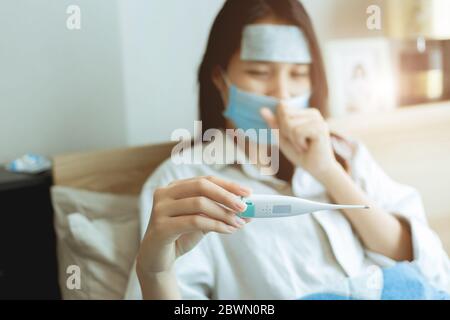 Femmes asiatiques regardant la température corporelle au thermomètre oral pour diagnostiquer la grippe à partir de coronavirus (Covid-19) infection autosoins rester à la maison. Banque D'Images