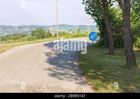 Une route asphaltée dans le pays de la campagne avec un signal circulaire bleu avec une flèche (Italie, Europe) Banque D'Images