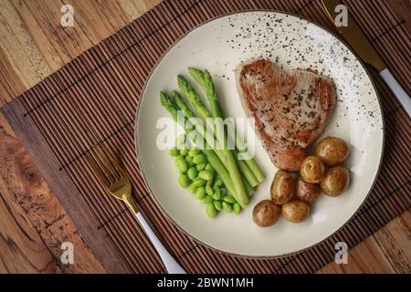 Steak de thon grillé servi avec asperges, pommes de terre rôties, haricots édamames et sauce hollandaise sur une assiette, vue du dessus Banque D'Images